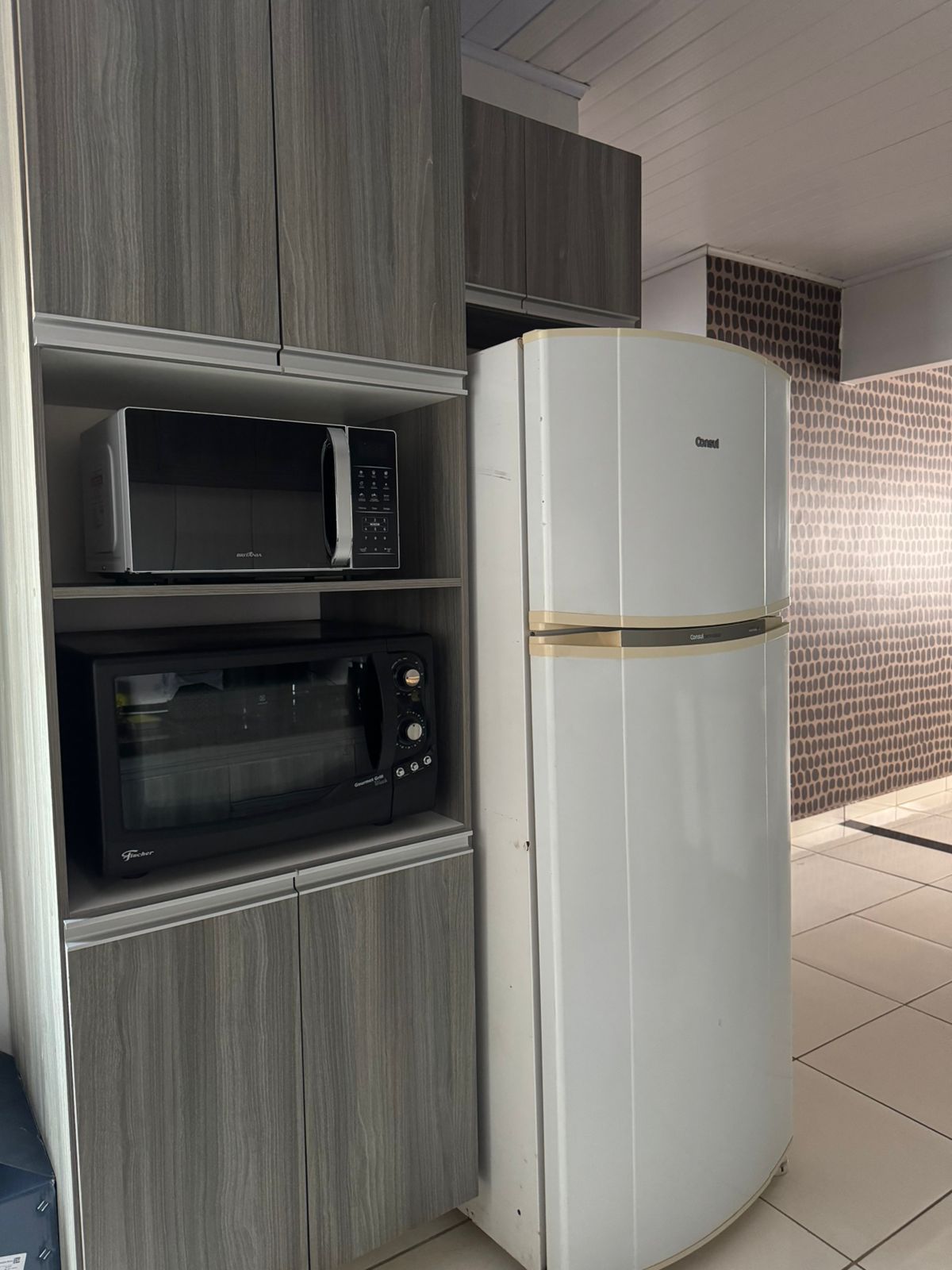 Eine Küche mit einem weißen Kühlschrank, einer schwarzen Mikrowelle und einem schwarzen Backofen.