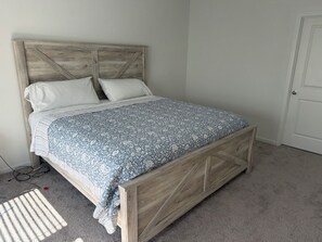 Un lit avec une tête de lit en bois, une couvre-lit à motifs et un sol recouvert d’une moquette.
