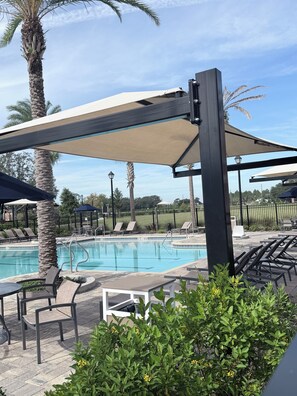 Un espace aménagé au bord de la piscine, avec des chaises longues, une piscine et des palmiers.