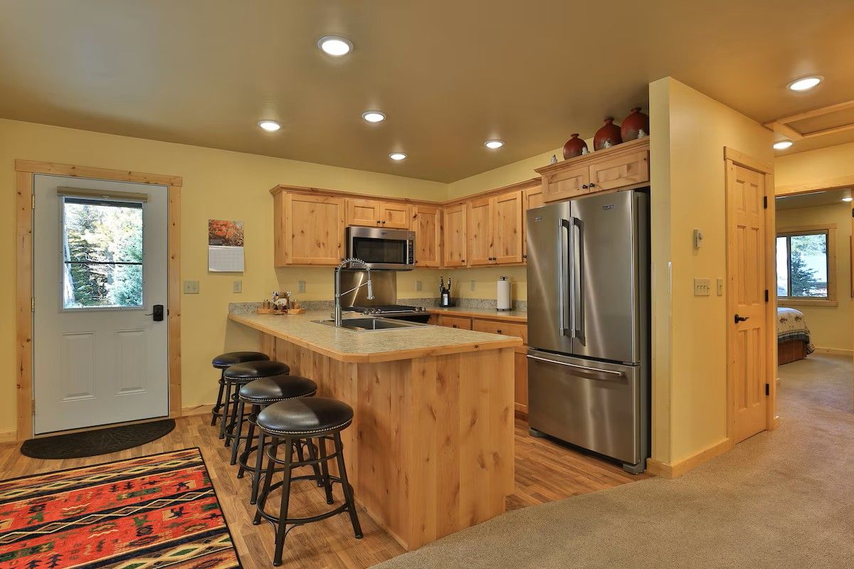 A kitchen with wooden cabinets, a stainless steel refrigerator, a microwave, and a bar stool area.