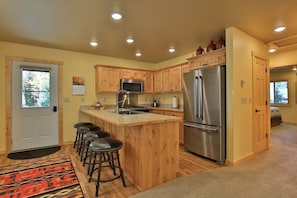 A kitchen with wooden cabinets, a stainless steel refrigerator, a microwave, and a bar stool area. - The Aspen Cabin (West Yellowstone)