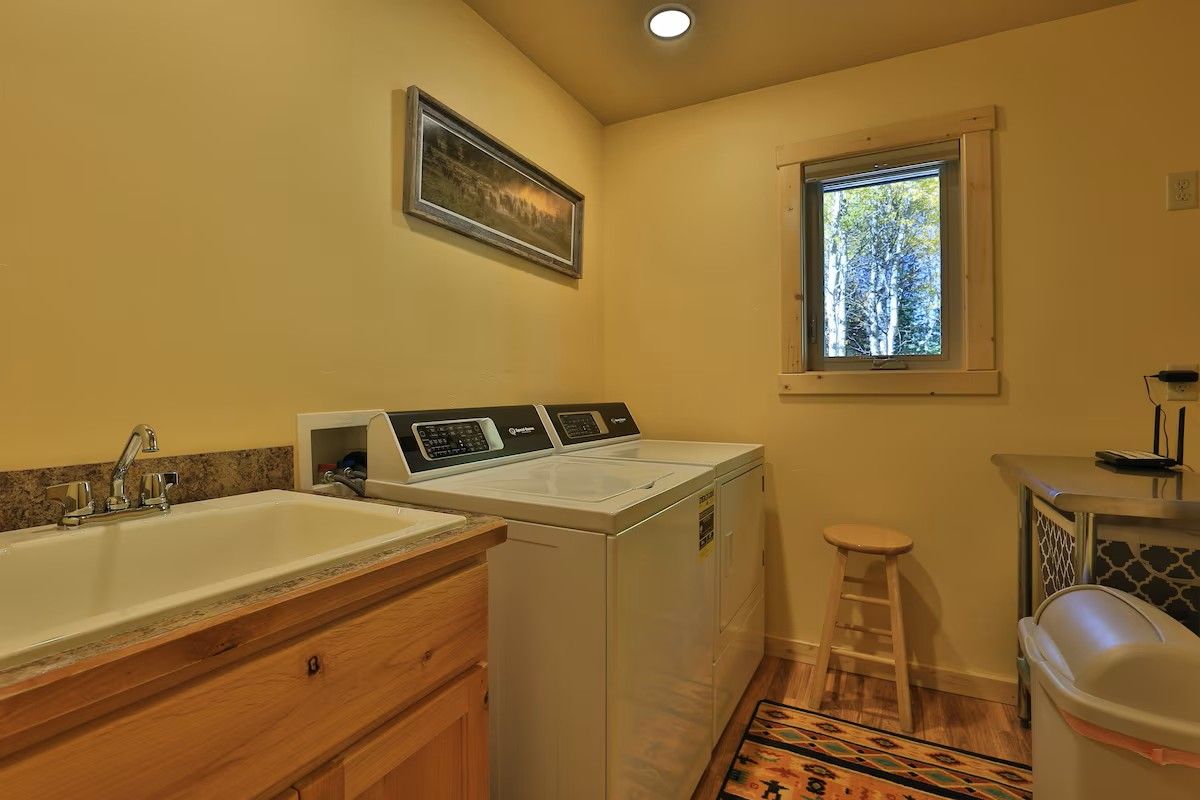 A laundry room with a washing machine, a sink, and a window.