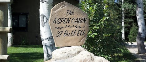 A wooden sign with the text 'The Aspen Cabin 37 Bull Elk' on a rock.