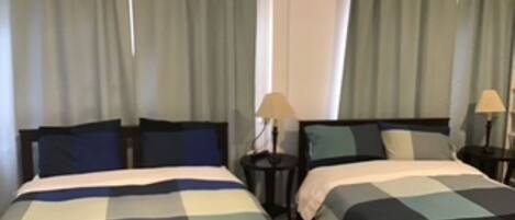 Ein Hotelzimmer mit zwei Betten, jeweils mit karierten Bettdecken, zwei Nachttischen mit Lampen und Vorhängen an den Fenstern.