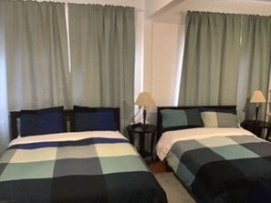 Une chambre d’hôtel avec deux lits, chacun recouvert d’une couvre-lit à carreaux, deux tables de chevet avec des lampes et des rideaux aux fenêtres.