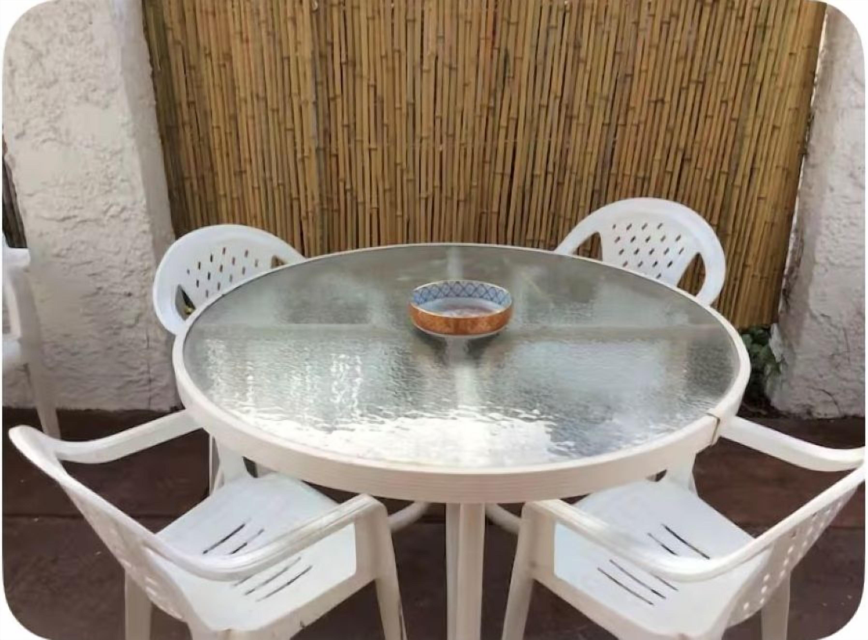 A round glass table with a bowl in the center, surrounded by four white plastic chairs.
