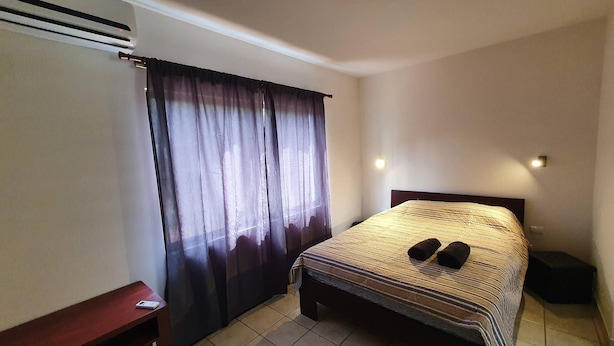 A small, tidy bedroom with a single bed, a wooden nightstand, a desk, and a window with curtains. - Marina Loft Studio Number 223 (Sardinal)