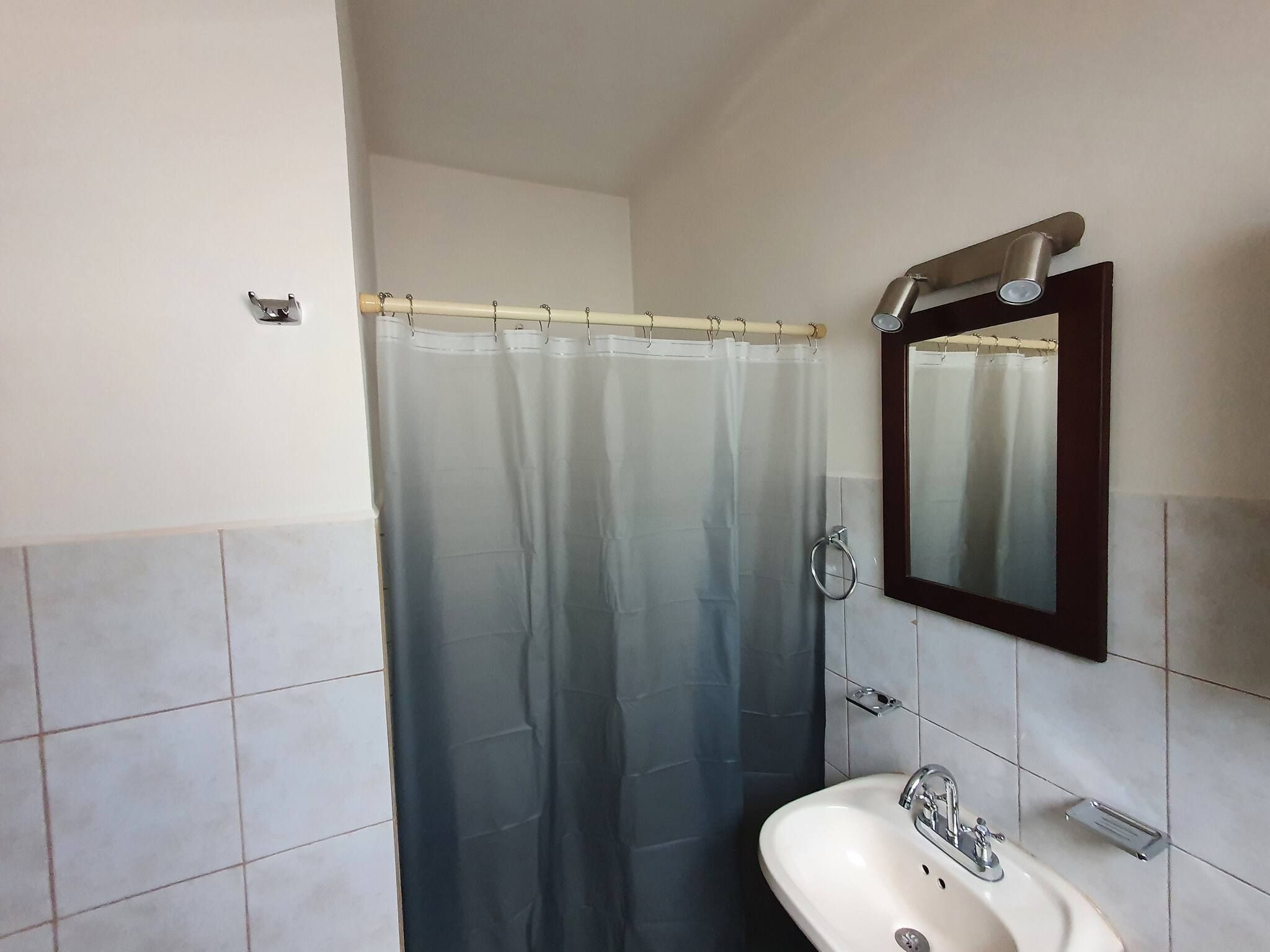 A bathroom with a shower curtain, a sink, and a mirror.