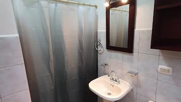 Un baño con cortina de ducha, lavamanos, espejo e inodoro.
