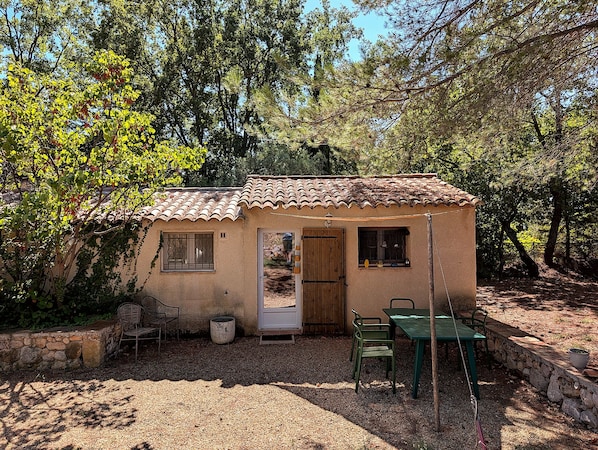 A small, single-story building with a tiled roof, a door, and a window. There is a table and two chairs outside. - Small stone house with a pool and pine forest – 10 minutes from Aix-en-Provence (Aix-en-Provence)