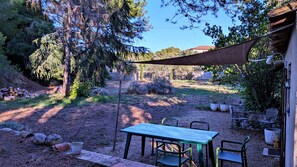An outdoor patio area with a table and chairs, surrounded by trees and a stone wall.