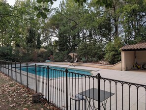 A swimming pool with a surrounding fence, a covered seating area, and a building with a tiled roof. - Small stone house with a pool and pine forest – 10 minutes from Aix-en-Provence (Aix-en-Provence)