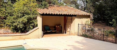 A swimming pool with a tiled deck, a covered seating area, and a fenced garden.