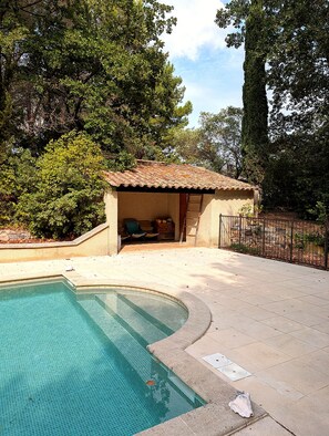 A swimming pool with a tiled deck, a covered seating area with chairs, and a fenced garden area. - Small stone house with a pool and pine forest – 10 minutes from Aix-en-Provence (Aix-en-Provence)