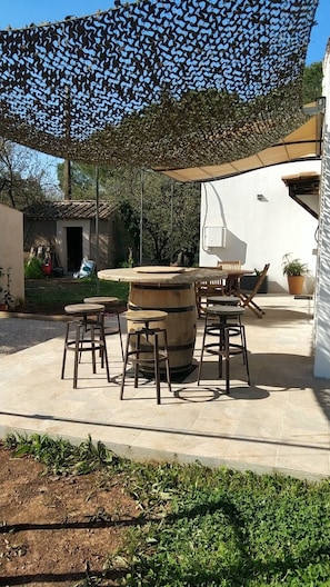 Een terras buiten met een ronde houten tafel, vier krukken en een barbecue.
