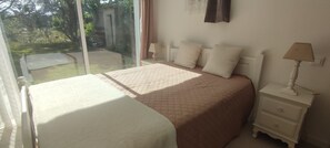 A bedroom with a large bed, a bedside table with a lamp, and a view of the garden through a glass door. - Villa unique ,piscine et foret (Gonfaron)