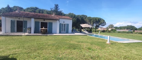A house with a swimming pool, a patio with outdoor furniture, and a lawn.