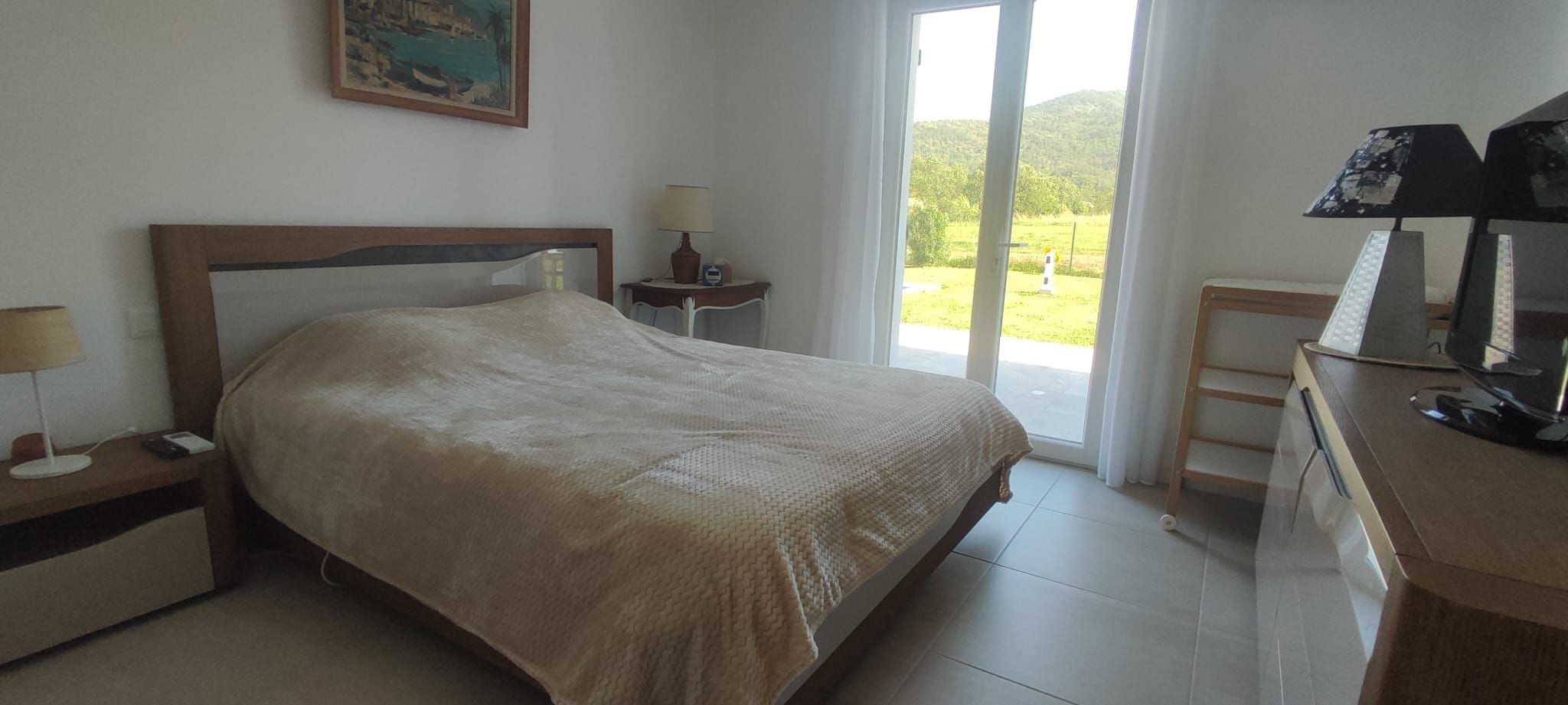 Une chambre à coucher comprenant un lit, des tables de chevet, un bureau et une fenêtre donnant sur un paysage verdoyant.