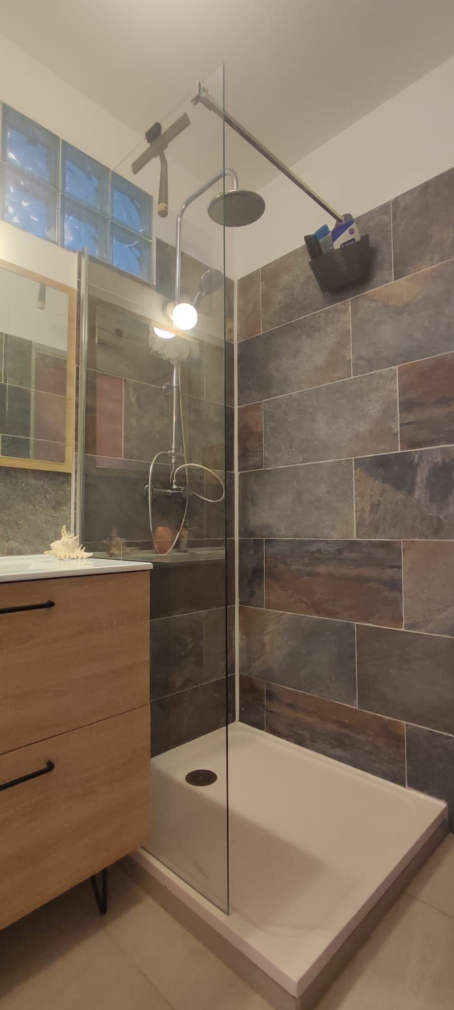 Um banheiro moderno com box de vidro, toucador de madeira e parede revestida de azulejos.