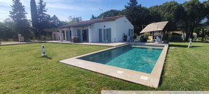A swimming pool with a tiled deck, surrounded by a grassy lawn and a white building with a red-tiled roof. - Villa unique ,piscine et foret (Gonfaron)