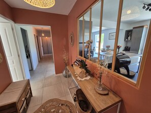 A well-lit hallway with a wooden bench, a mirror reflecting a dining area, and a door leading to another room. - Villa unique ,piscine et foret (Gonfaron)