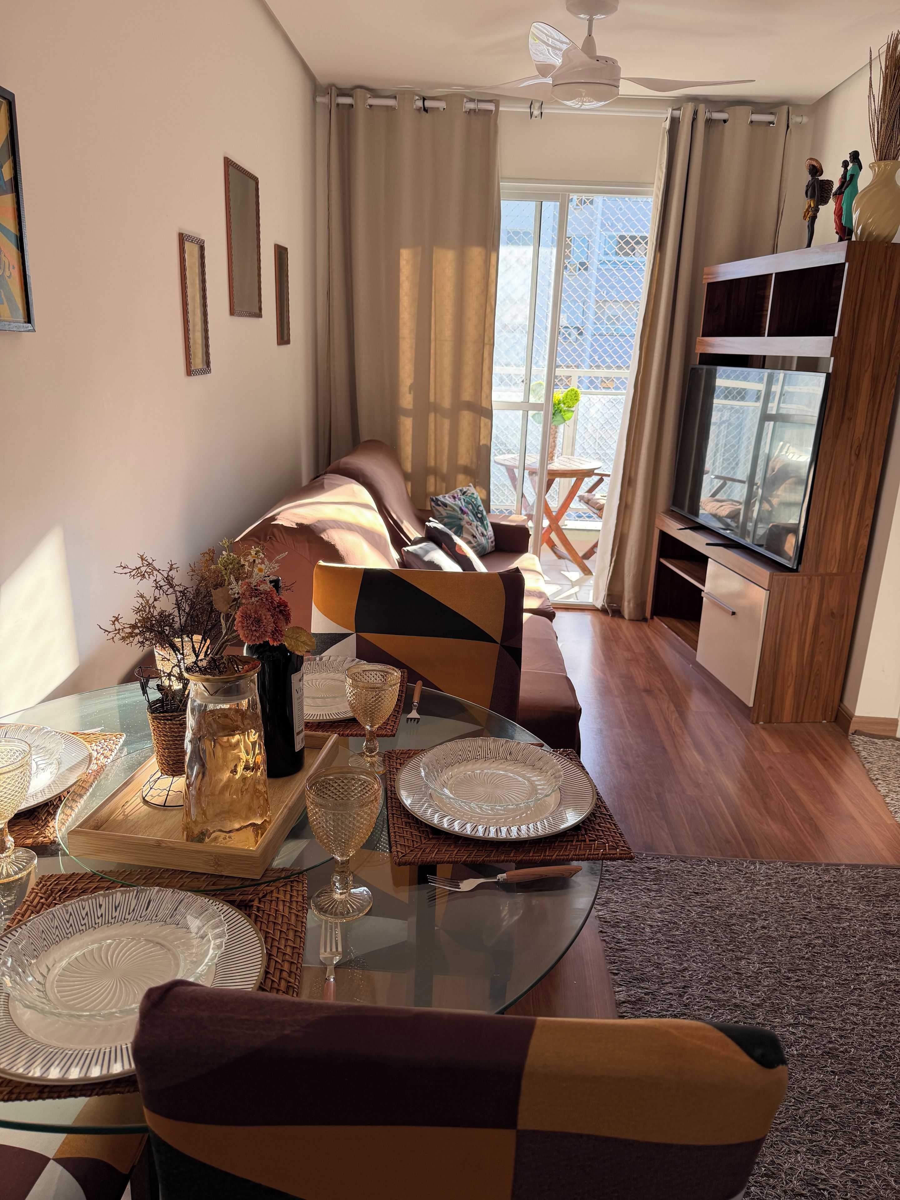 Un coin repas avec une table en verre dressée pour deux personnes, un canapé et un téléviseur en arrière-plan.