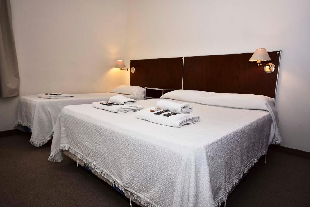 A hotel room with two beds, each with a white bedspread and pillows, and a wooden headboard.