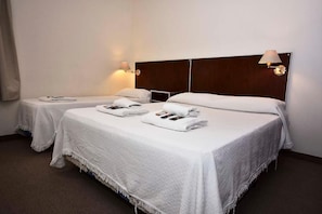 Een hotelkamer met twee bedden, elk met een witte spreidek en kussens, en een houten hoofdbord.