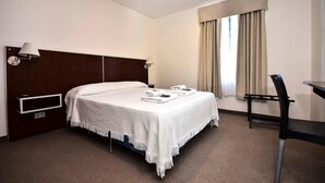 A hotel room with a bed, a desk, a chair, a lamp, and a window with curtains. - Hotel Playa (Comodoro Rivadavia)