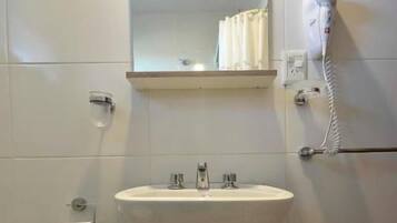 Un baño con un lavabo blanco, un espejo encima, un perchero y un secador de pelo en la pared.
