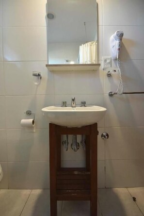 Een badkamer met een wit wastafelmeubel, een spiegel erboven, een handdoekrek en een haardroger aan de muur.