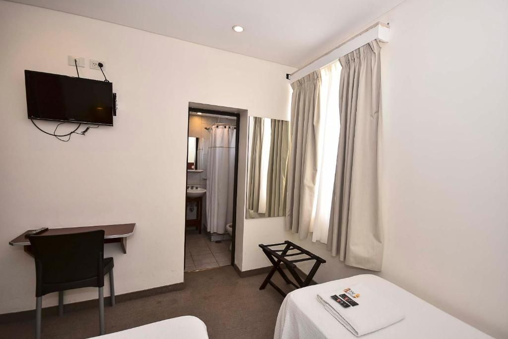 Une chambre d’hôtel avec un lit, un bureau, une chaise, un téléviseur fixé au mur et une salle de bain visible à travers une porte ouverte.