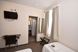 Habitación de hotel con cama, escritorio, silla, televisor montado en la pared y baño visible a través de una puerta abierta.
