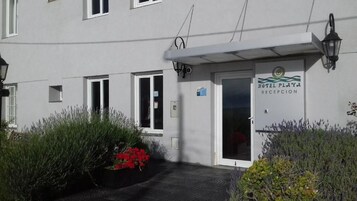 Recepção de hotel com fachada branca, porta com placa e uma pequena janela.