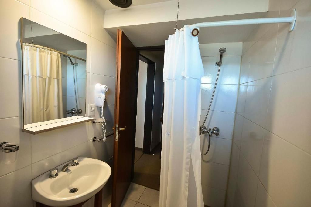 A bathroom with a sink, mirror, shower, and a door leading to another room.