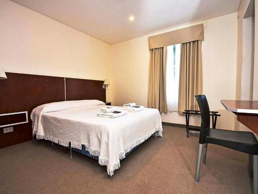 Een hotelkamer met een bed, nachtkastje, stoel en bureau.
