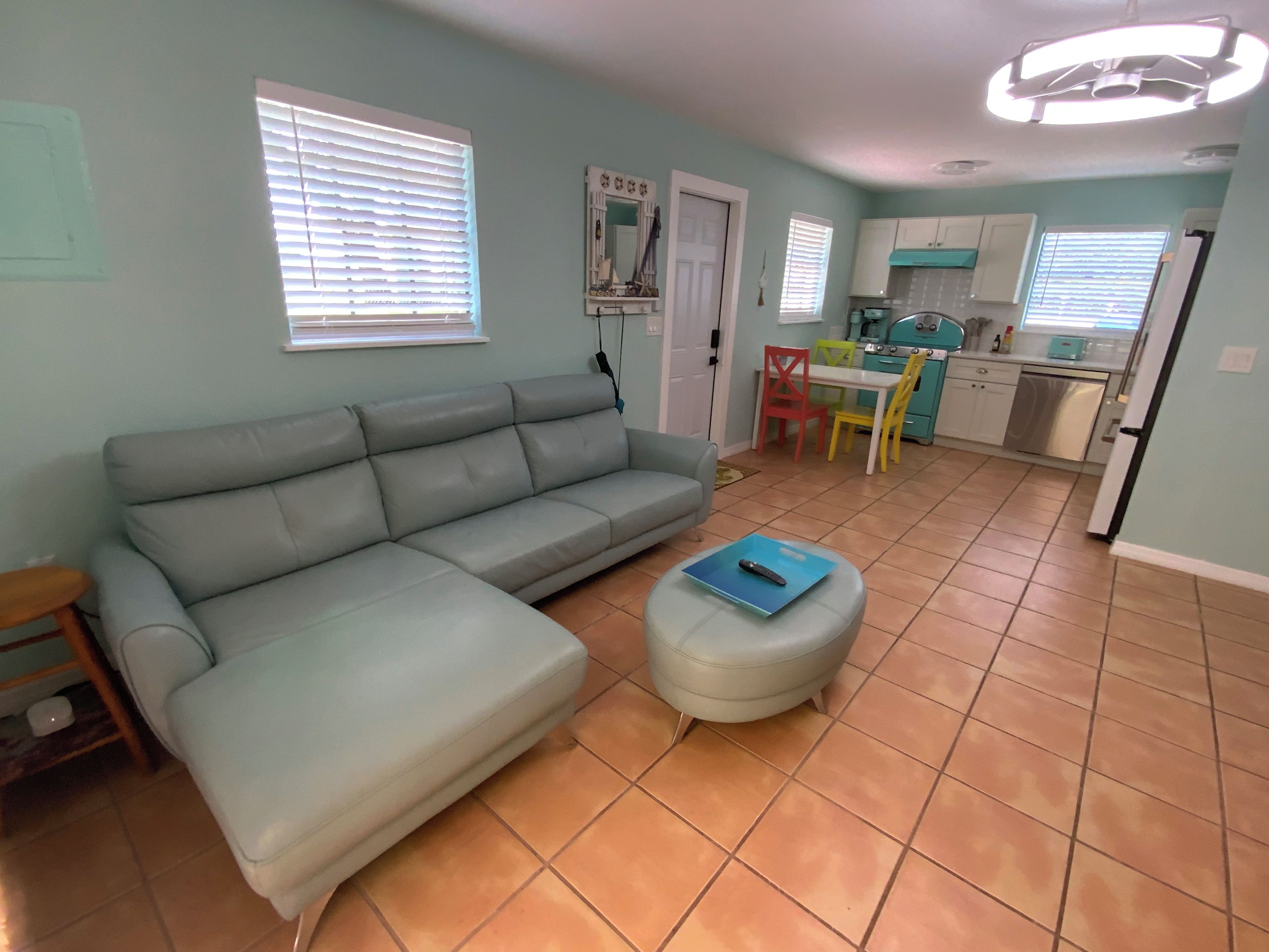 Un salon avec un canapé, un pouf et une télécommande posée sur le pouf.