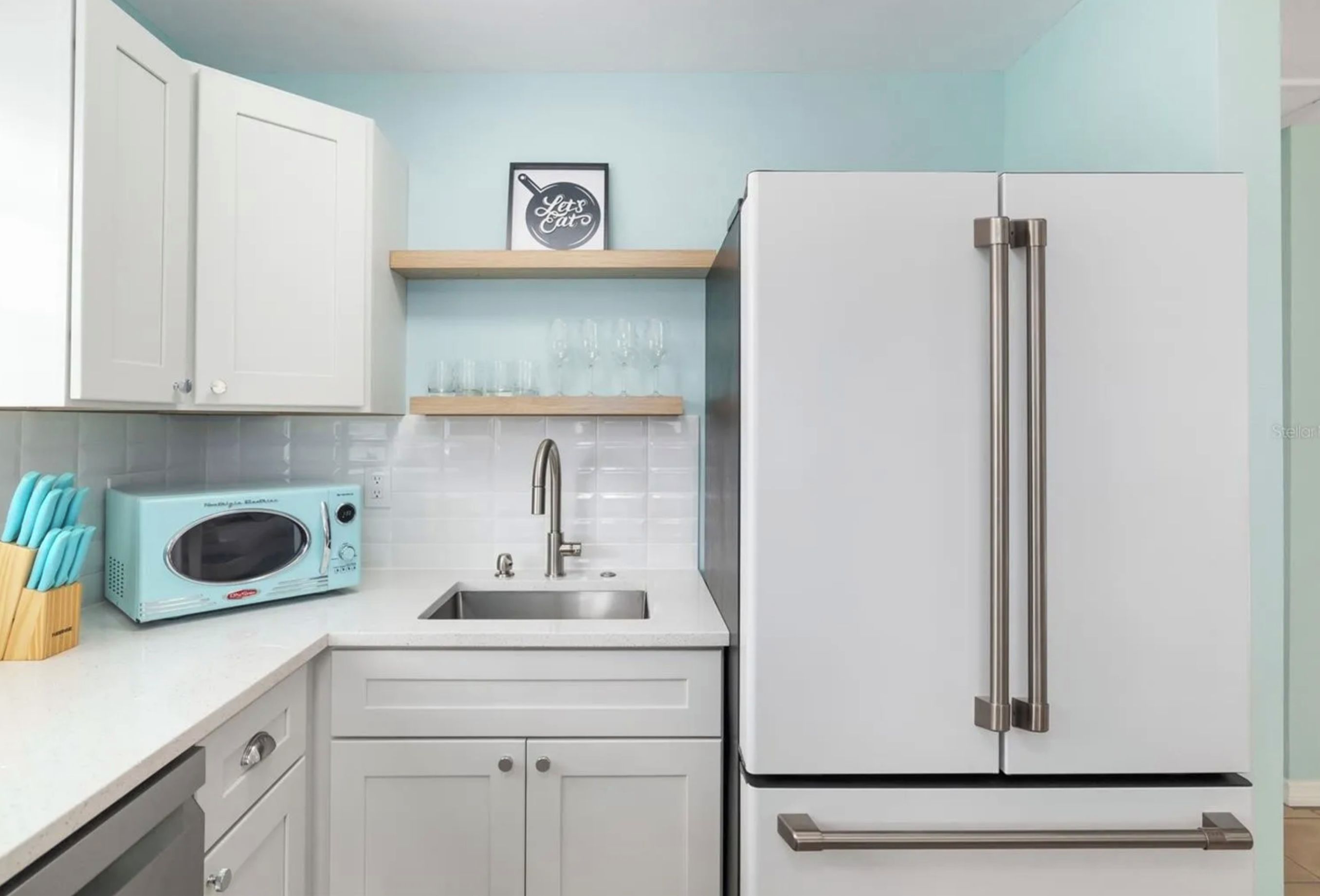 A kitchen with white cabinets, a microwave, a sink, and a stainless steel refrigerator.