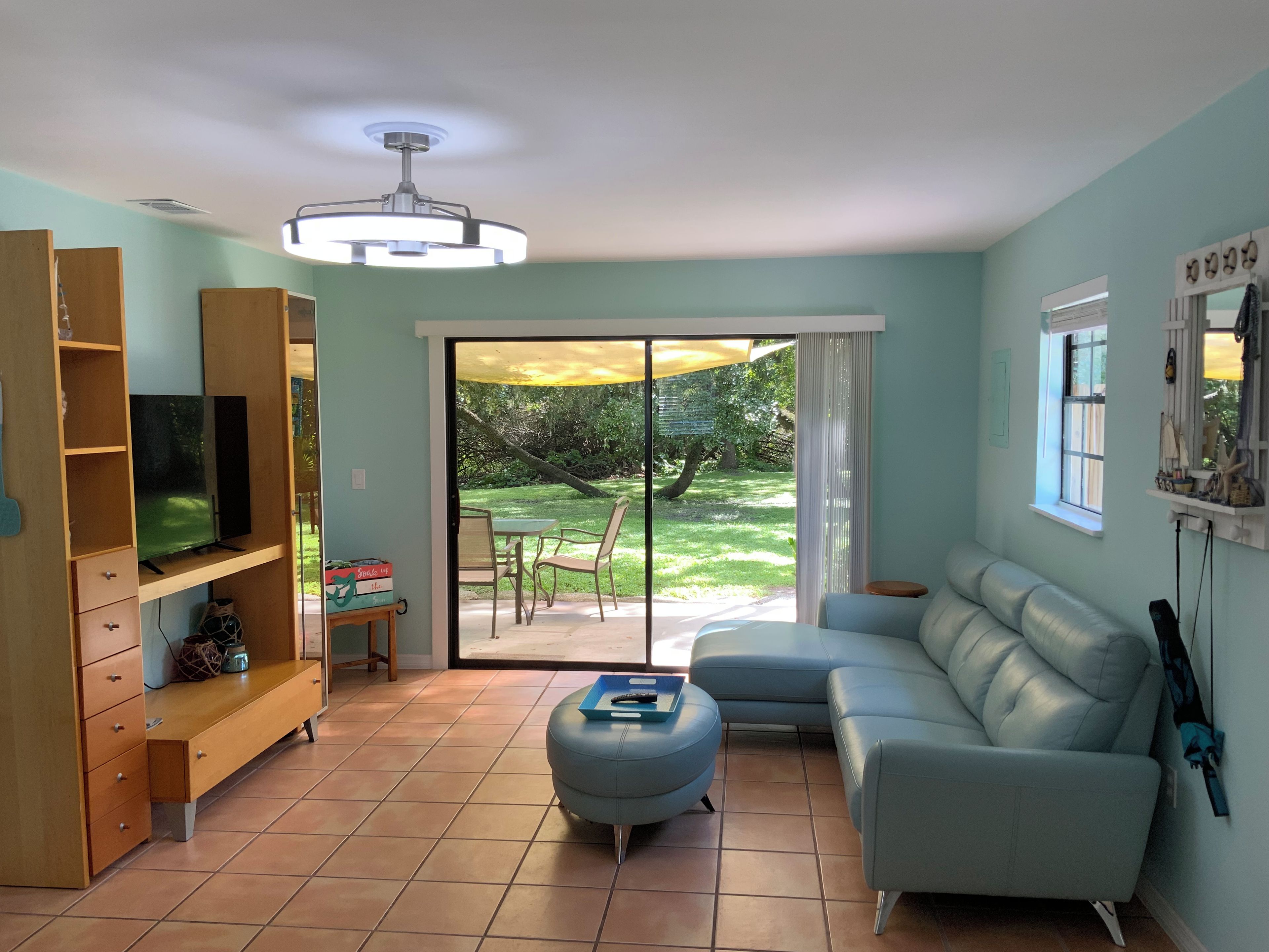 A living room with a television, sofa, ottoman, and a sliding glass door leading to a patio.