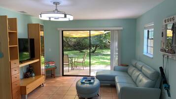 A living room with a television, sofa, ottoman, and a sliding glass door leading to a patio.