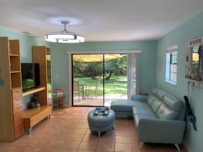 A living room with a television, sofa, ottoman, and a sliding glass door leading to a patio.