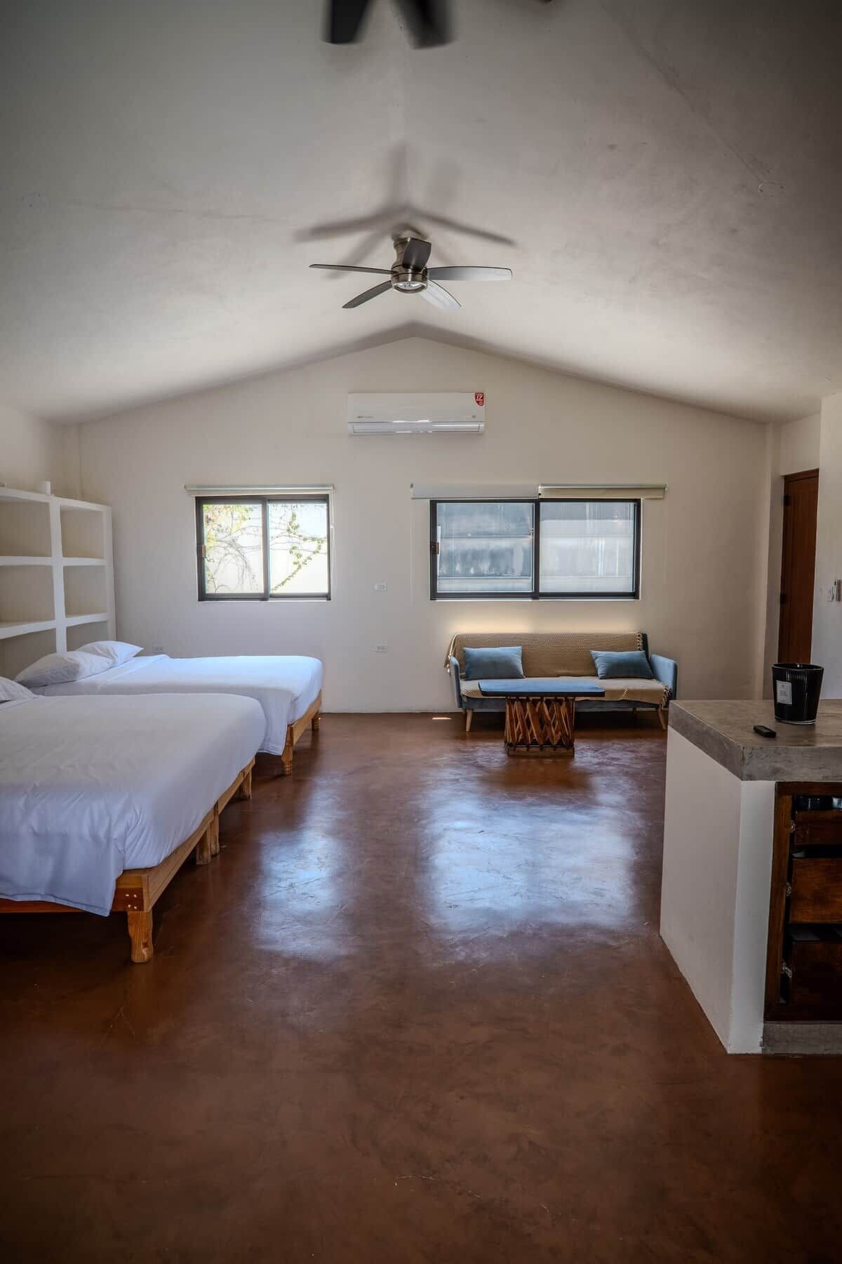 Une chambre avec deux lits, un canapé, un ventilateur de plafond et une fenêtre.