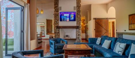 A living room with a stone fireplace, blue sofas, and a television mounted on the wall.