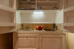 Eine Küche mit Holzschränken, einer Spüle aus Edelstahl und einer Arbeitsplatte mit verschiedenen Gegenständen, darunter eine Flasche, ein Glas und einige Gemüsesorten.