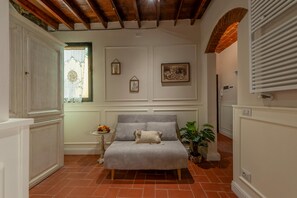Ein Schlafzimmer mit einem Bett, einem kleinen Tisch mit Früchten, einer Topfpflanze und einem Fenster mit Vorhängen.