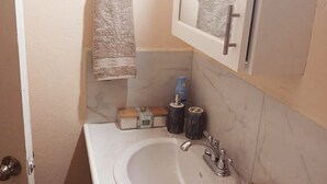Casa de banho com lavatório branco, espelho e duas toalhas penduradas em suportes metálicos.