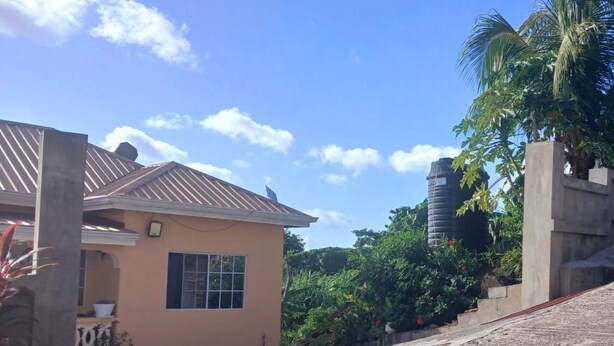 Uma casa residencial com telhado inclinado, uma janela e uma escadaria de concreto que dá acesso a um nível superior.