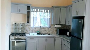 Cozinha com armários brancos, fogão, geladeira e janela com cortinas.