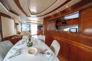 A dining area with a table set for four, a vase with flowers, and a view of the sea through the windows. - Barans Boat (Göcek)
