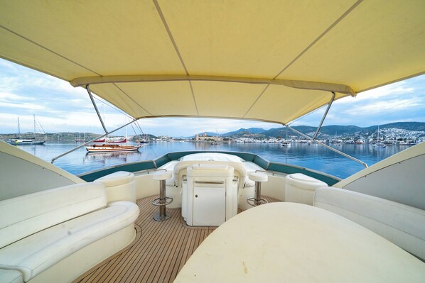 A boat deck with seating, a canopy, and a view of a marina with boats and buildings.